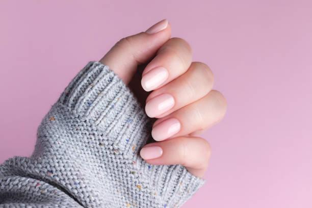 Hand in sweater with nude nails on pink background Female hand in gray knitted sweater with natural beautiful manicure - pink nude nails on pink background. Nail care concept Gel Nail  stock pictures, royalty-free photos & images