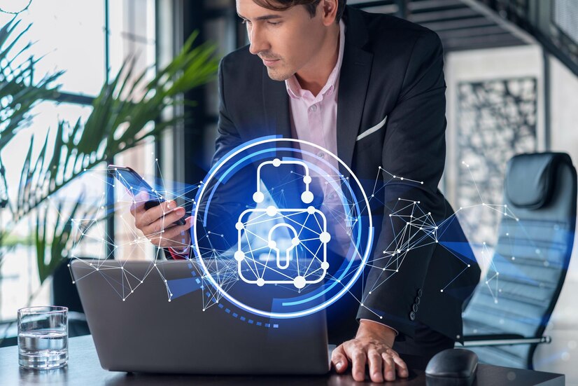 A person in a suit working at a desk with a laptop and holding a smartphone.