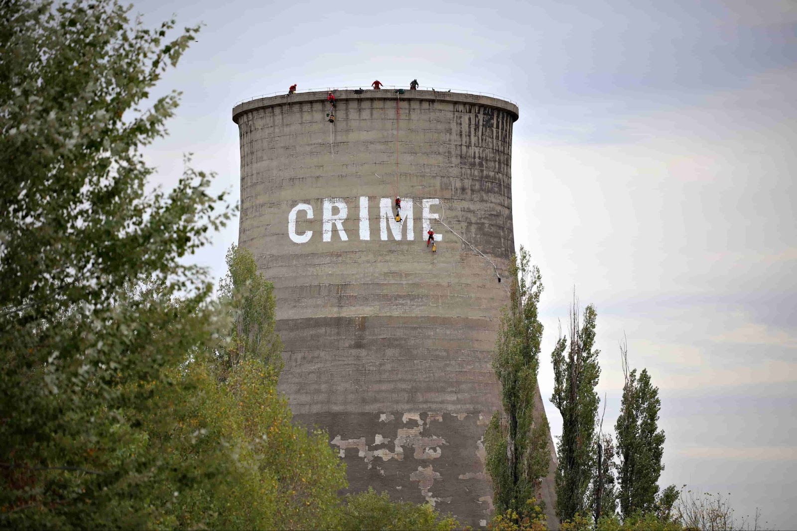 A giant power plant chimney has the word CRIME painted on it by activists using climbing gear