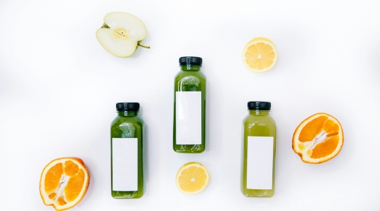 Green detox juice bottles with lemons, apples, and oranges on a white background