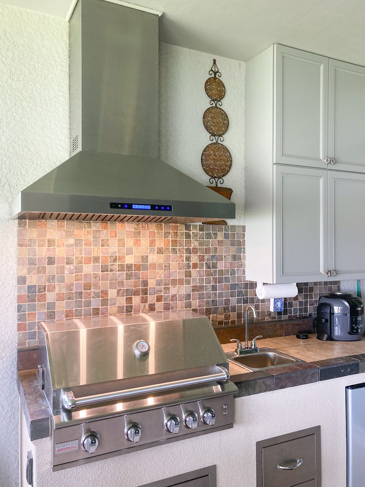 Warm kitchen design featuring a stainless steel Proline range hood, colorful backsplash, and decorative wall art for a homey touch - prolinerangehoods.com