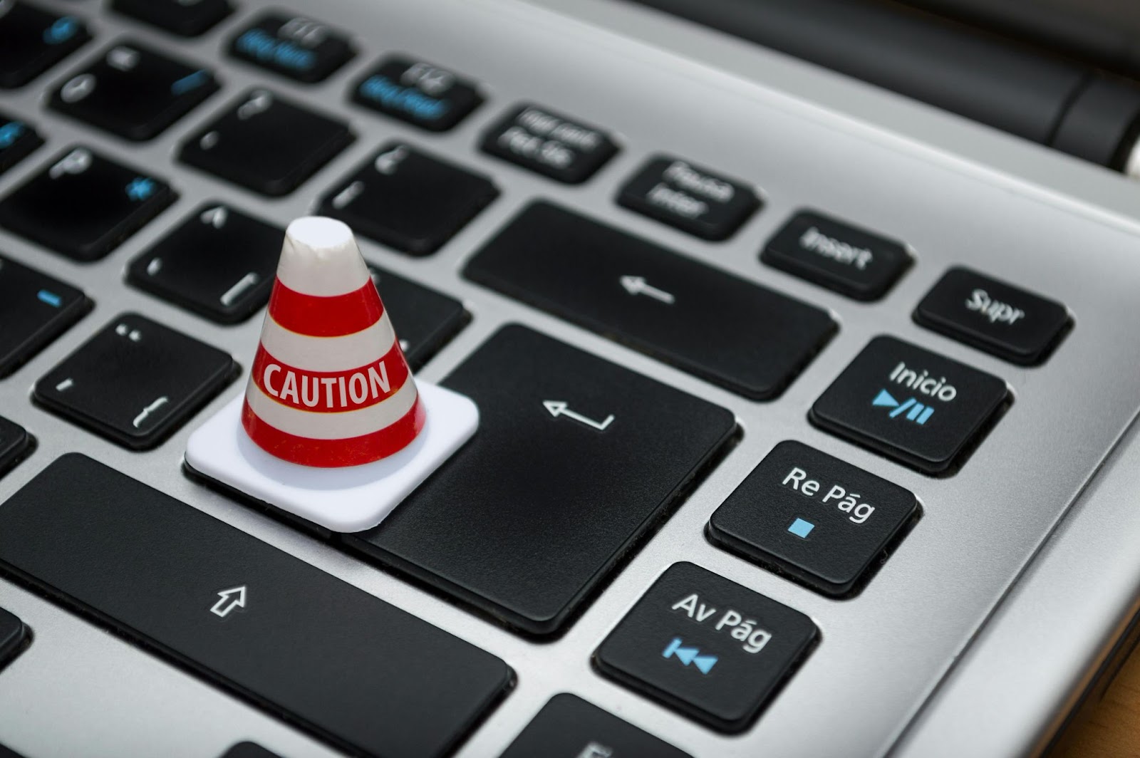 Miniature traffic cone with 'CAUTION' text placed on a laptop keyboard, symbolizing the need for caution to prevent data theft