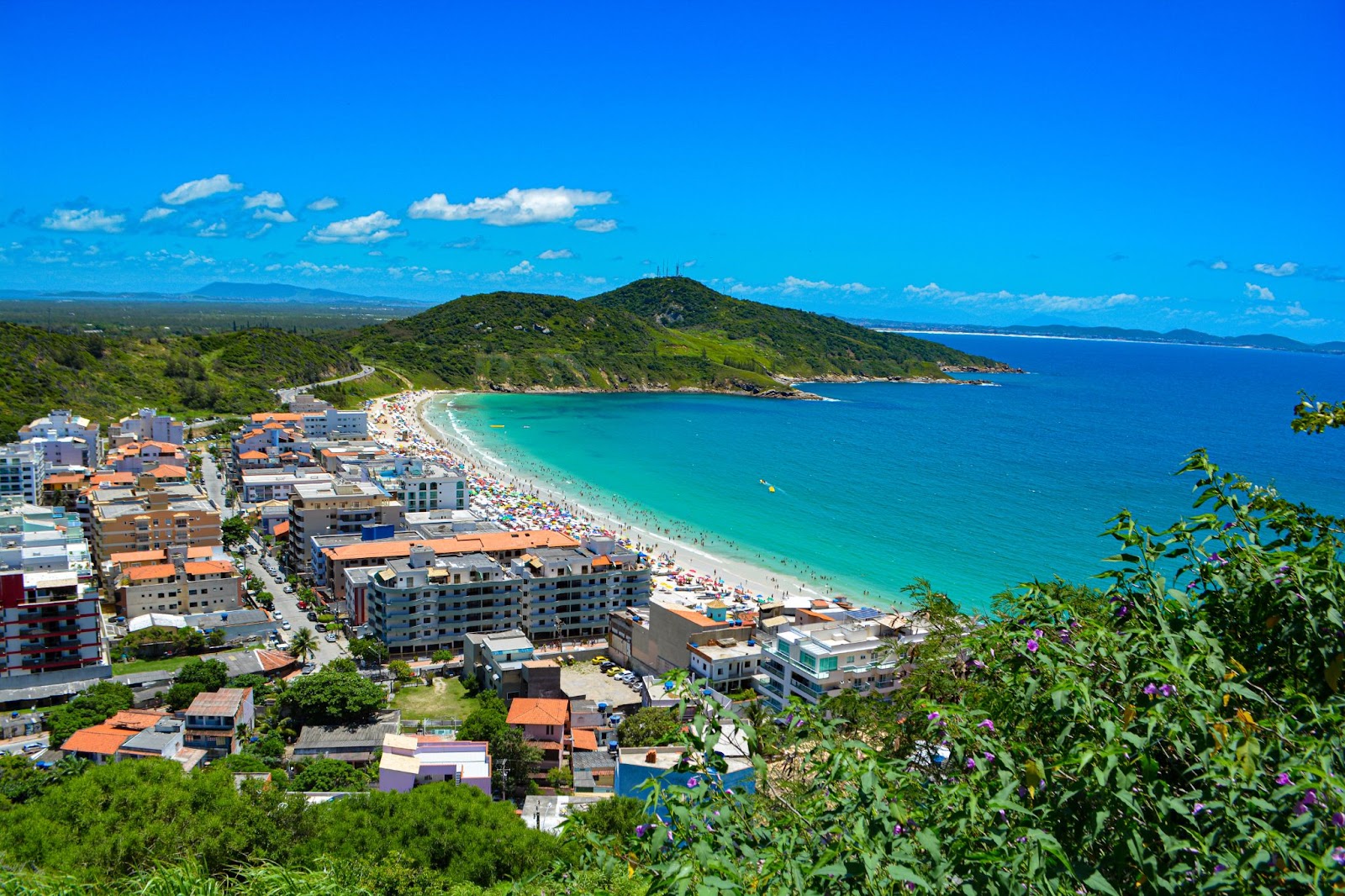 Orla de Prainha. Pequena praia em Arrial. Com prédios e casas em contraste com a vegetação e as pessoas que estão na areia