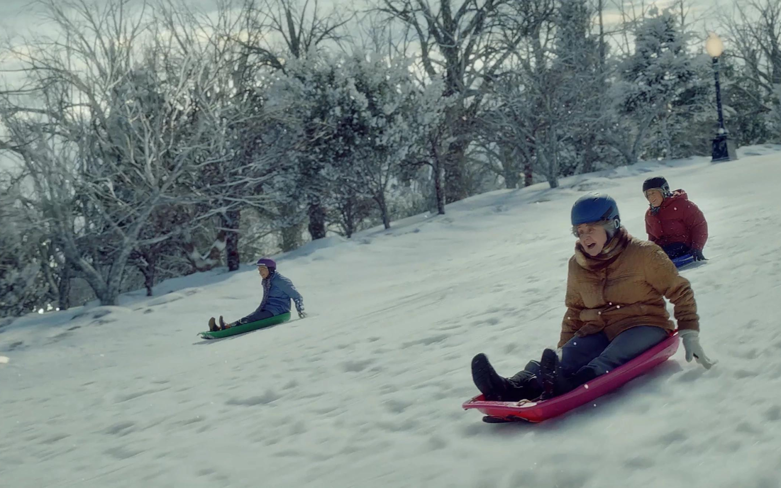 A couple of people sledding down a snowy hillDescription automatically generated