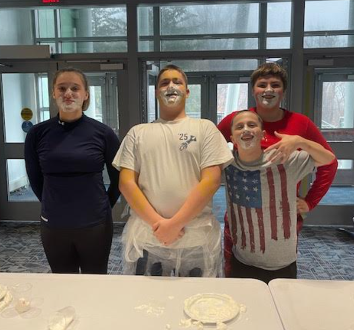 Students with whipped-cream on their faces celebrate after completing the contest.