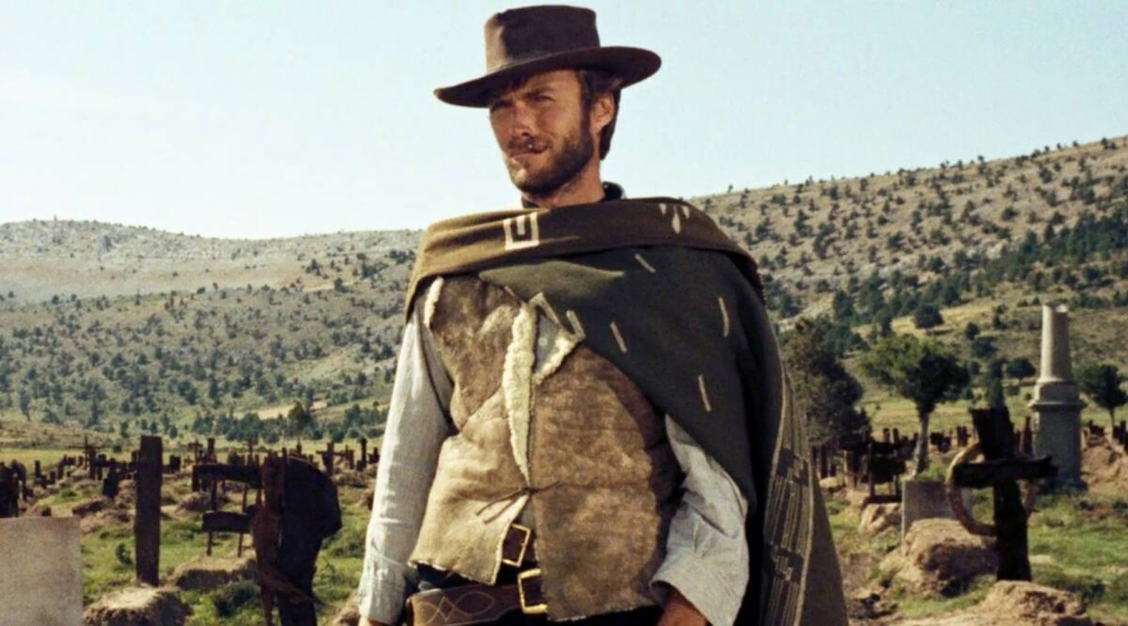 Clint Eastwood en una escena clásica de una película del género western, con su característico sombrero, poncho y fondo de un paisaje desértico.