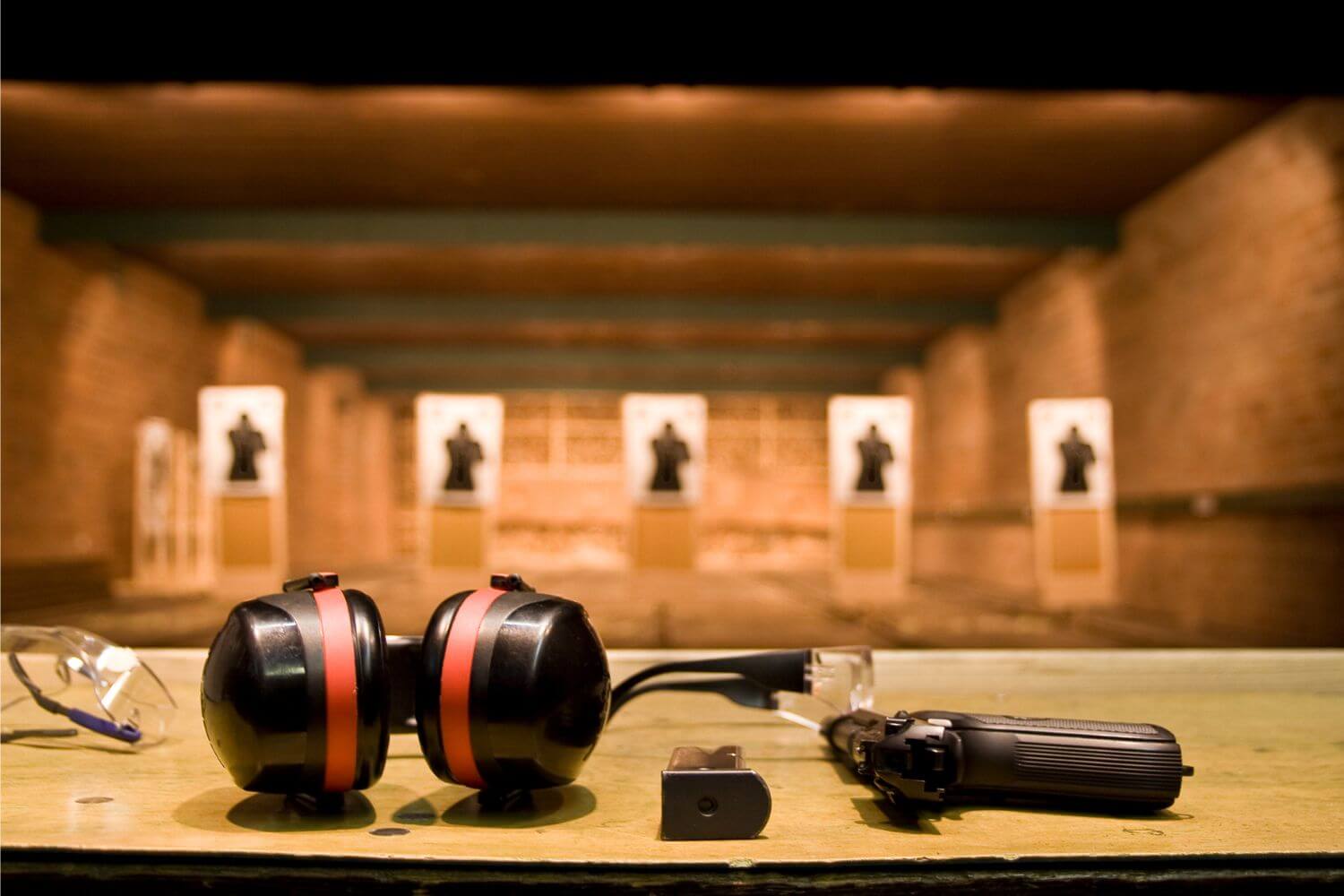 Handgun, magazine, protective eyewear and glasses sit on a booth at an indoor shooting range