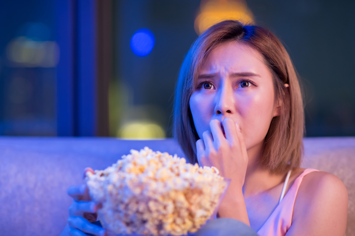mulher comendo pipoca e assustada assistindo filmes de terror 