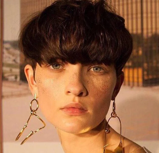 a lady with a model-like face and statement earrings wearing a choppy bowl cut.