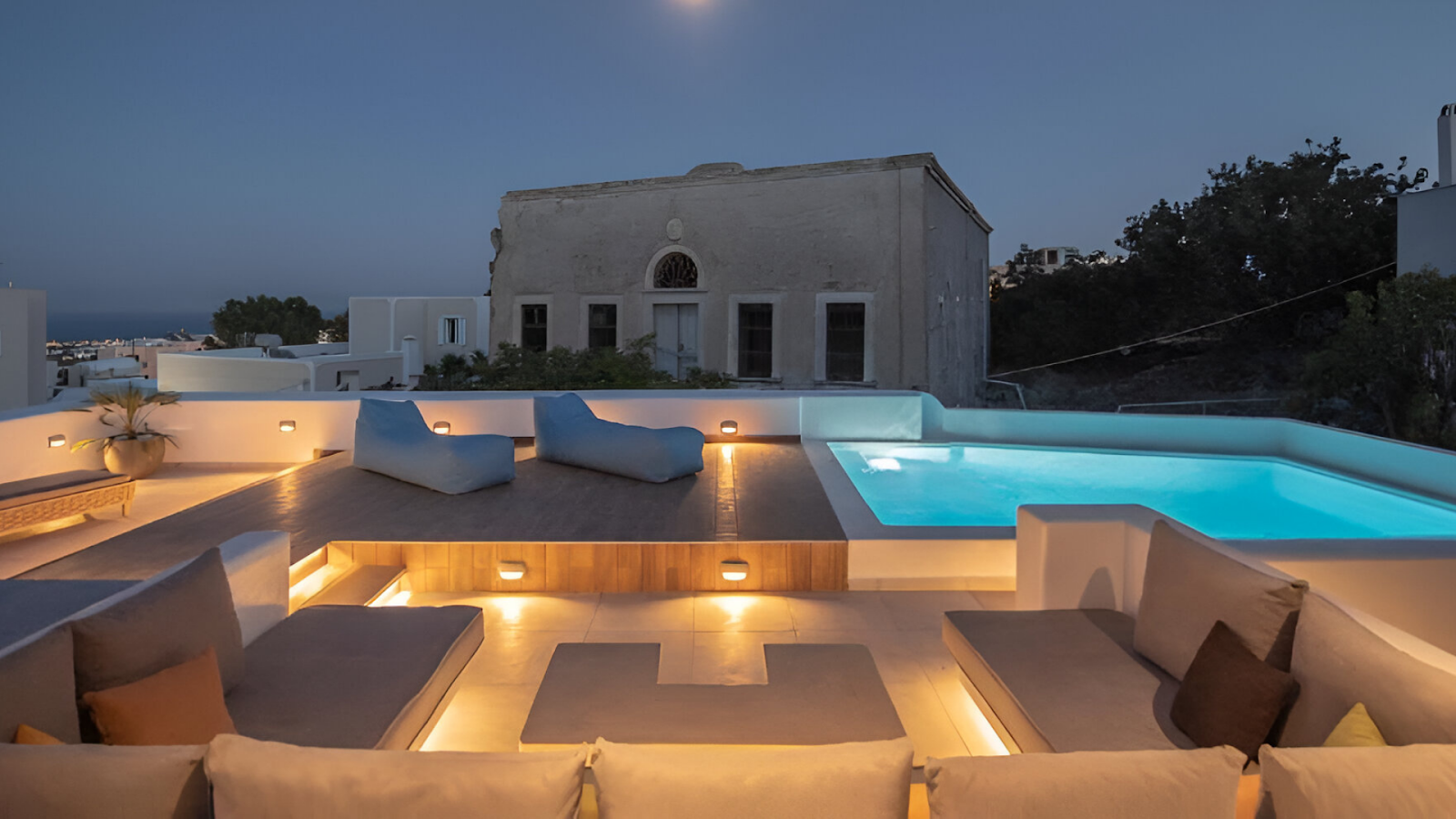 Couches and sun loungers beside the pool of a luxury villa in Santorini.