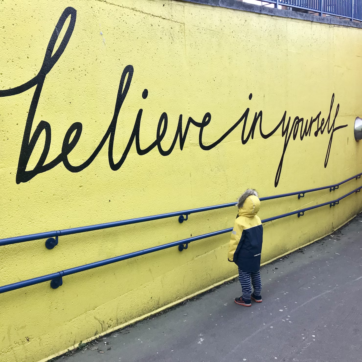 A Kid is Looking at the Writing on a Wall, 'Believe in Yourself'
