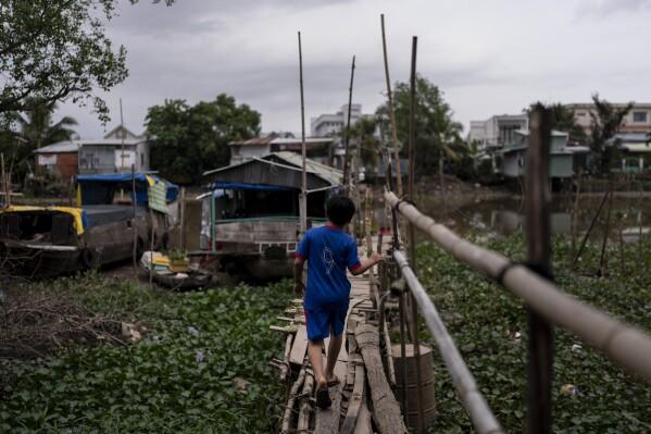 Do Hoang Trung walks along a weathered bridge built with bamboo poles and wooden planks to reach a houseboat he shares with his twin sister and their grandmother in Can Tho, Vietnam, Tuesday, Jan. 16, 2024. After their mother left to pursue better financial opportunities in Ho Chi Minh City, the twins remained in the care of their grandmother, who supports the family by selling steamed buns at a floating market. (AP Photo/Jae C. Hong)