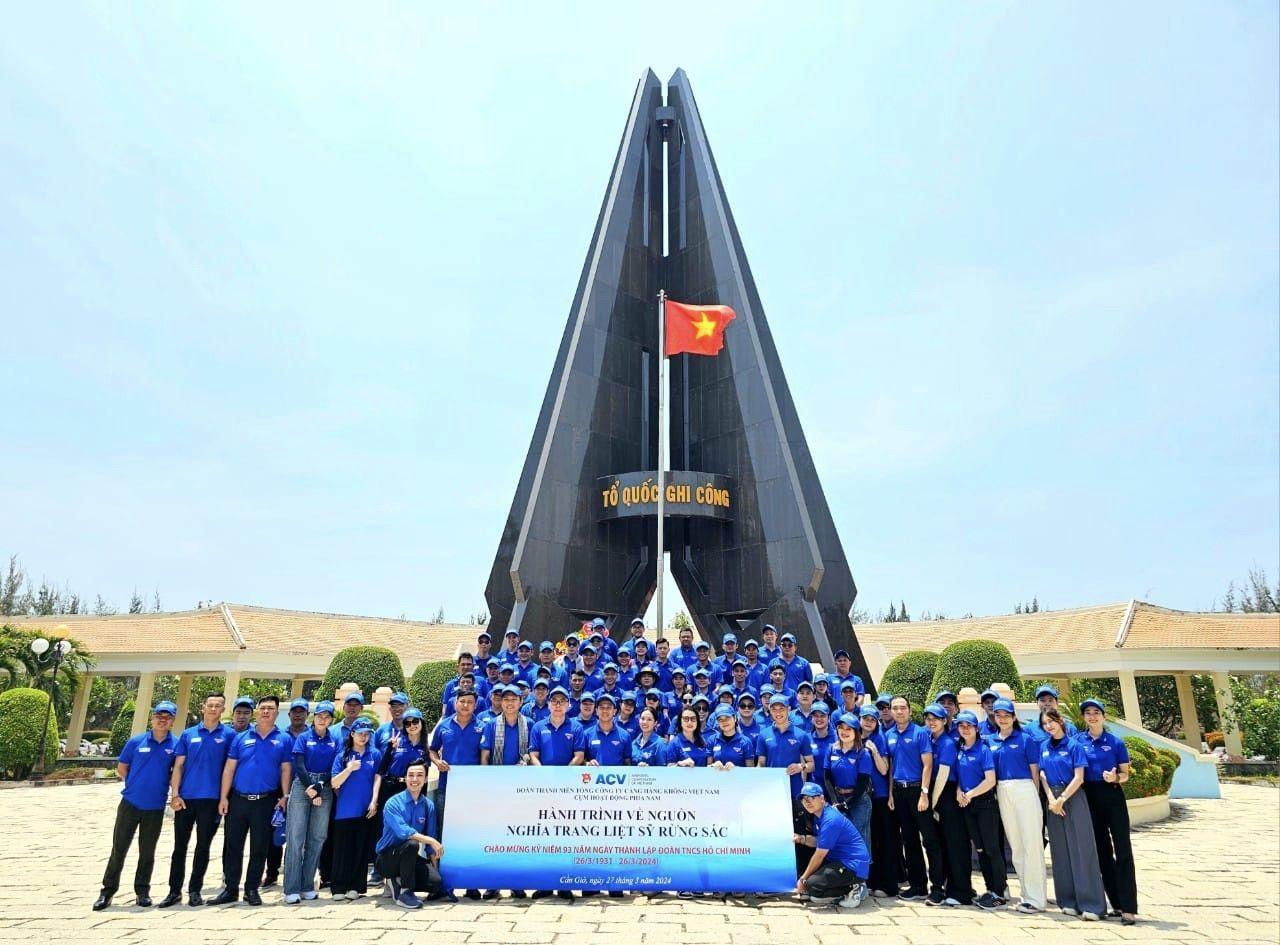 A group of people in blue shirts posing for a photo with Ryugyong Hotel in the backgroundDescription automatically generated