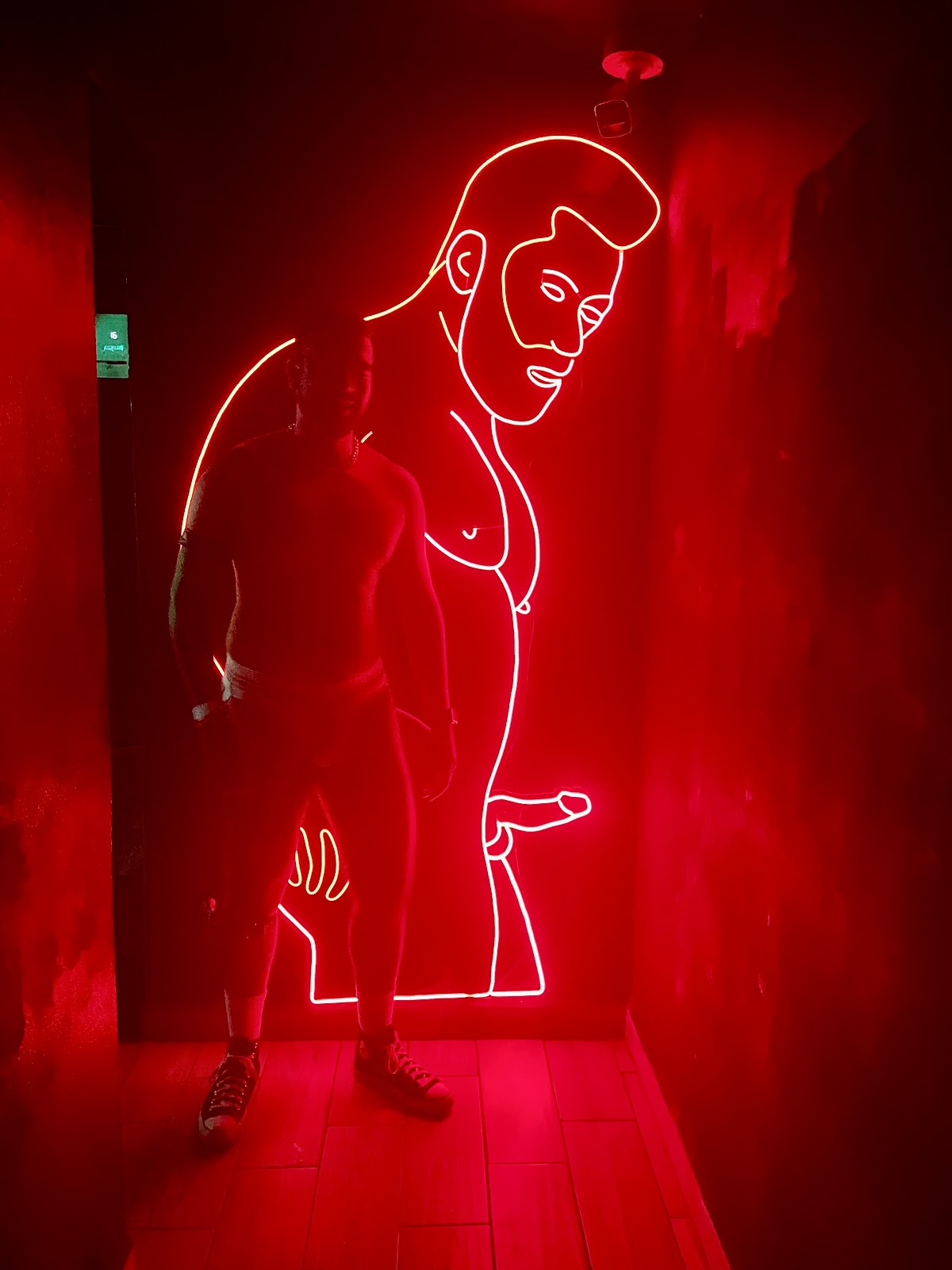gay male in underwear in gay night club standing in front of a neon light sign of a gay leather bear daddy showing off his cut erect cock