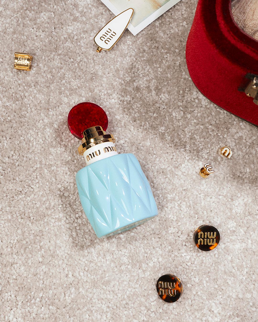 A blue bottle of perfume next to a red hat

Description automatically generated