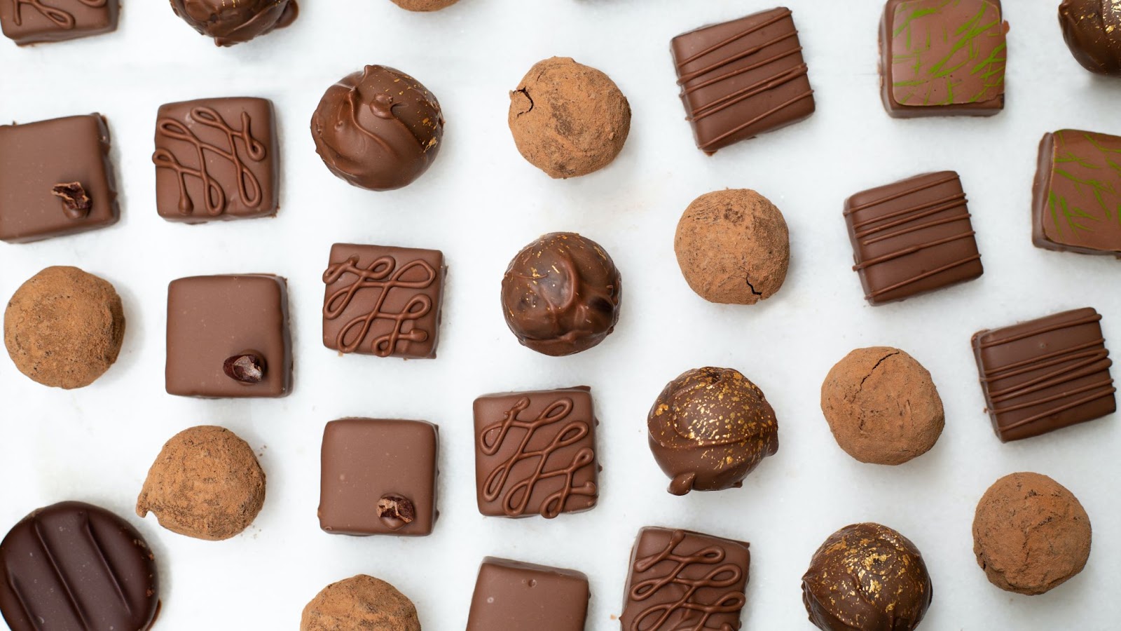 a top-down view of assorted chocolates on a white countertop, laid out in a grid pattern, highlighting Karat Chocolate Boutique and Cafe, one of Kelowna's best dessert shops