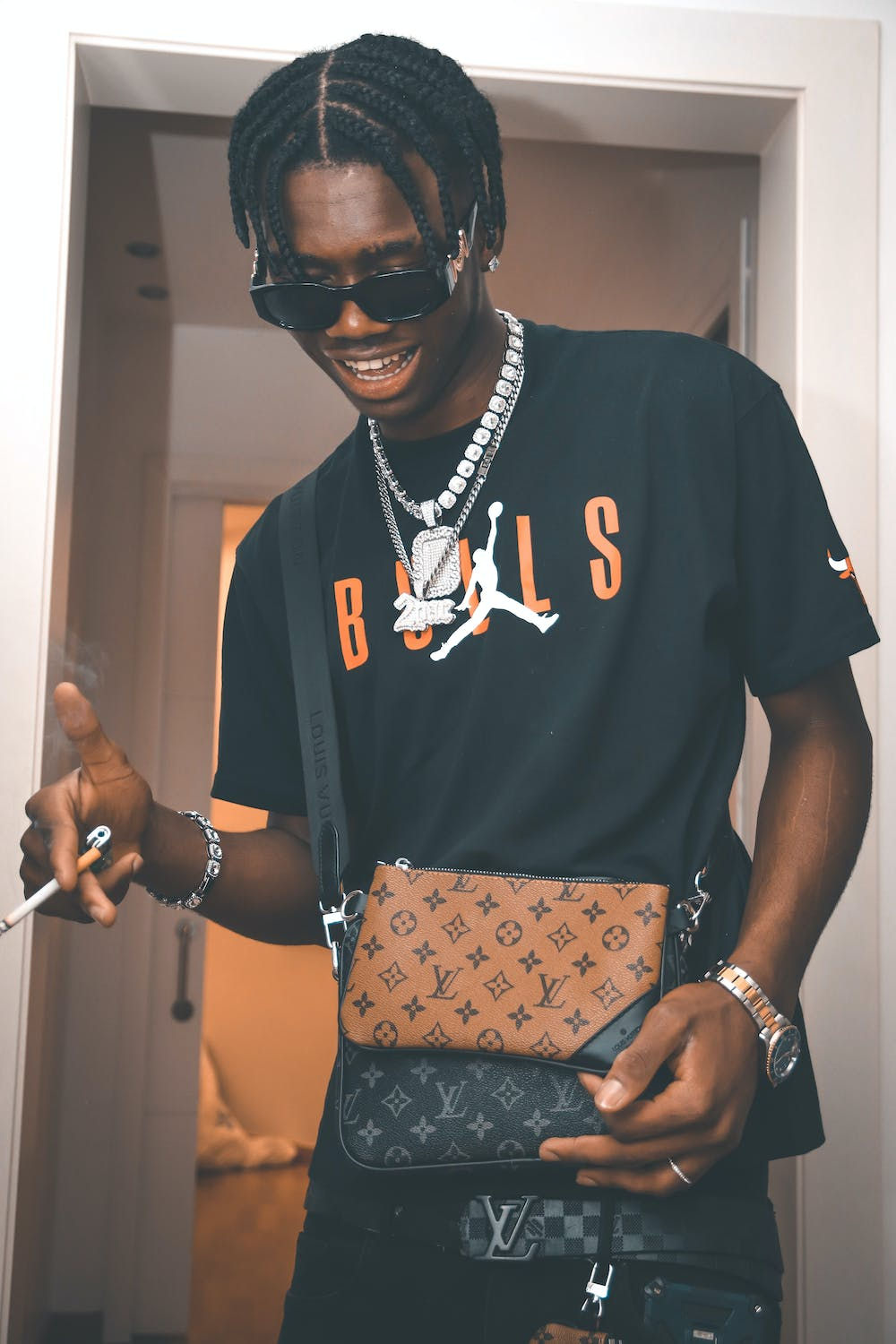 A man in sunglasses wearing chains and carrying an LV bag.