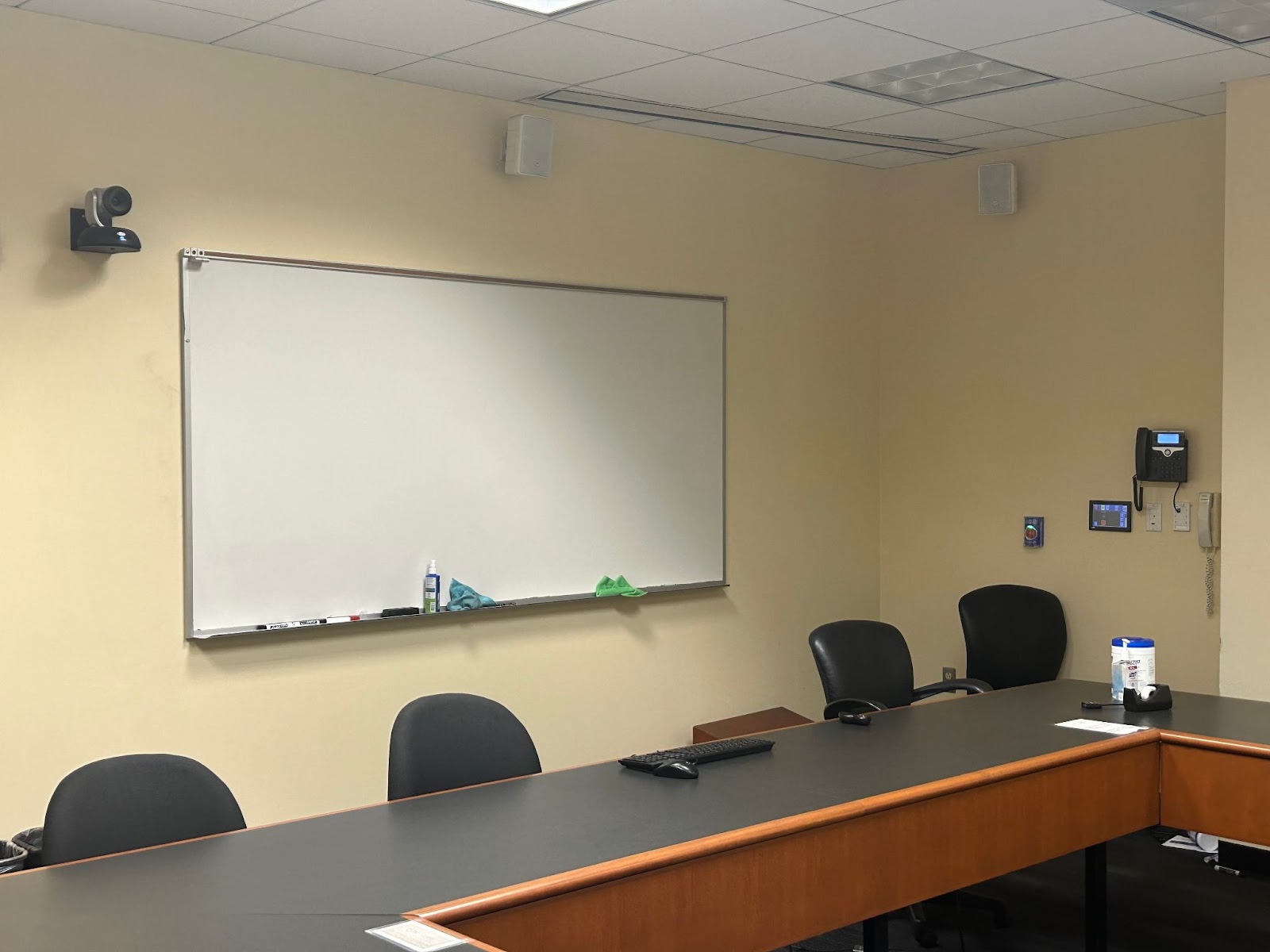View of the front of the room: Camera, keyboard and mouse, hotline phone, touch control panel, projector screen area.