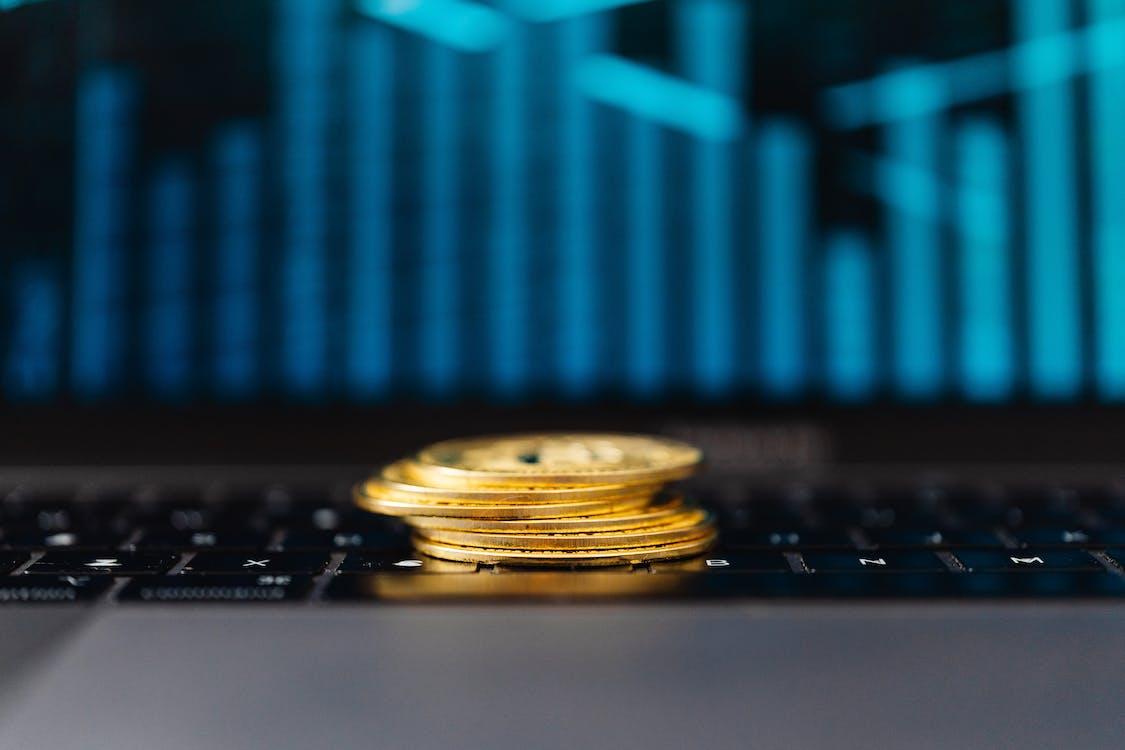 Free Stack of Gold Coins on a Laptop Displaying a Graph Stock Photo