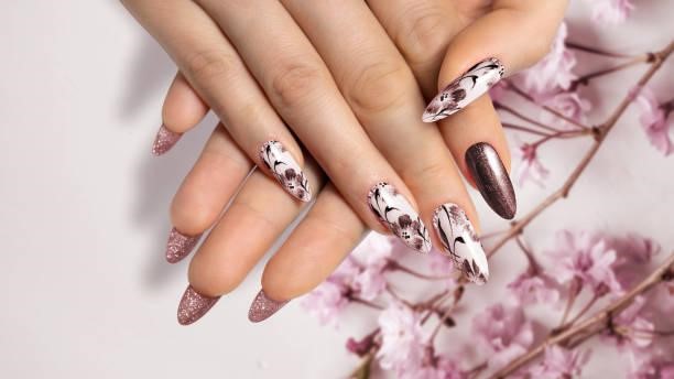 Close-up of a brown manicure on long, sharp nails on a flower background with a painted flower design. Flower nail design. Brown manicure on sharp long nails close-up on a flower background with painted flower design. Nail Art Designs  stock pictures, royalty-free photos & images