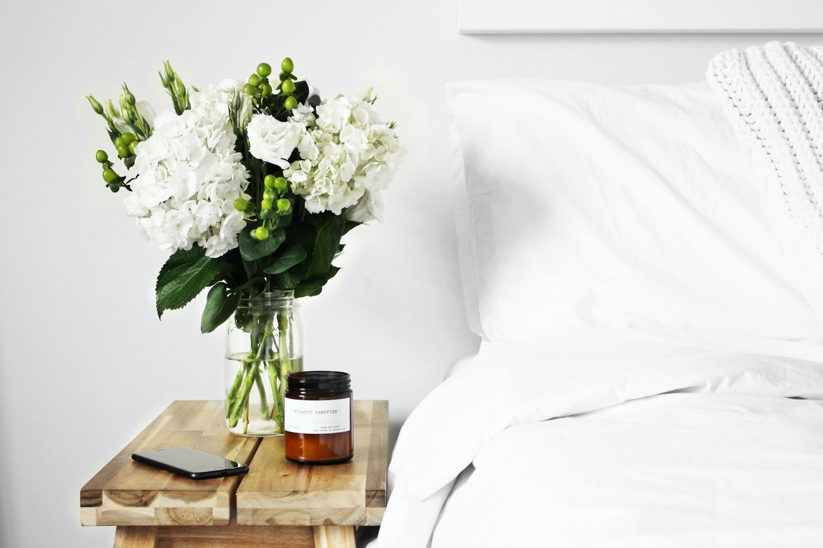 White flowers in a vase next to bedside table in bedroom