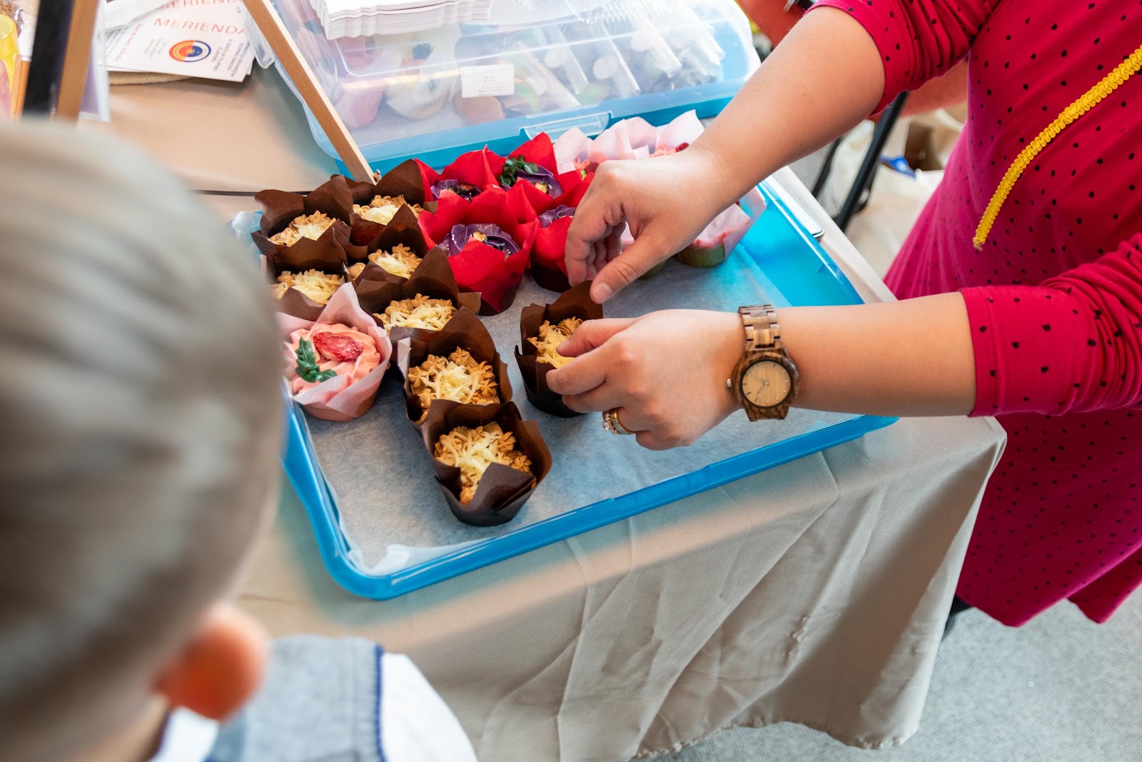 A person's hands reaching for cupcakesDescription automatically generated