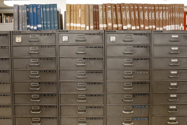 A row of gray filing cabinets with rows of labeled binders on top.