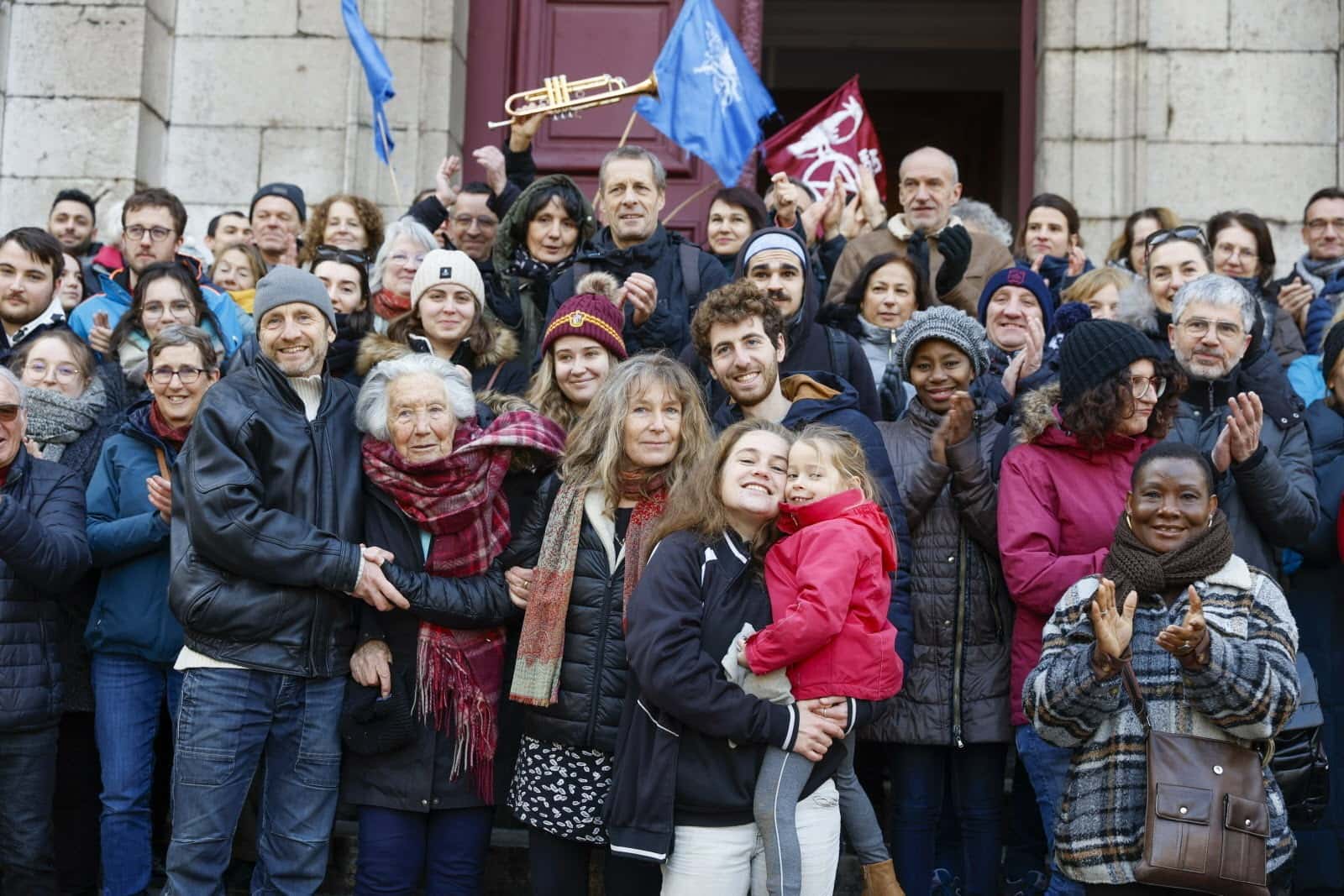 Coline smiles while holding up a young relative and behind her is stood dozens of family members and supporters 