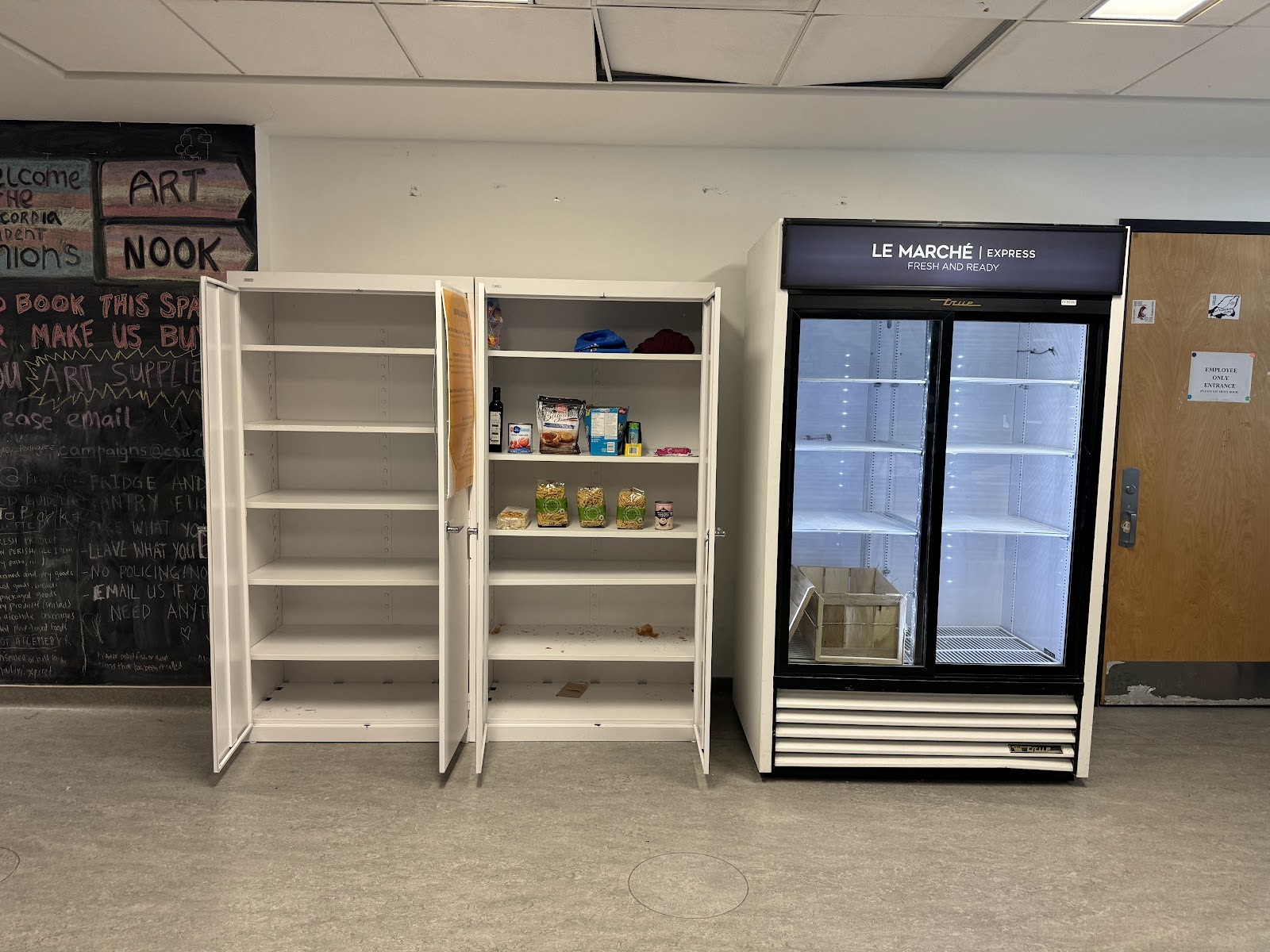 Two tall, white cabinets with the doors open to reveal some groceries like pasta and snacks on the shelves. To the right, there is an empty fridge.