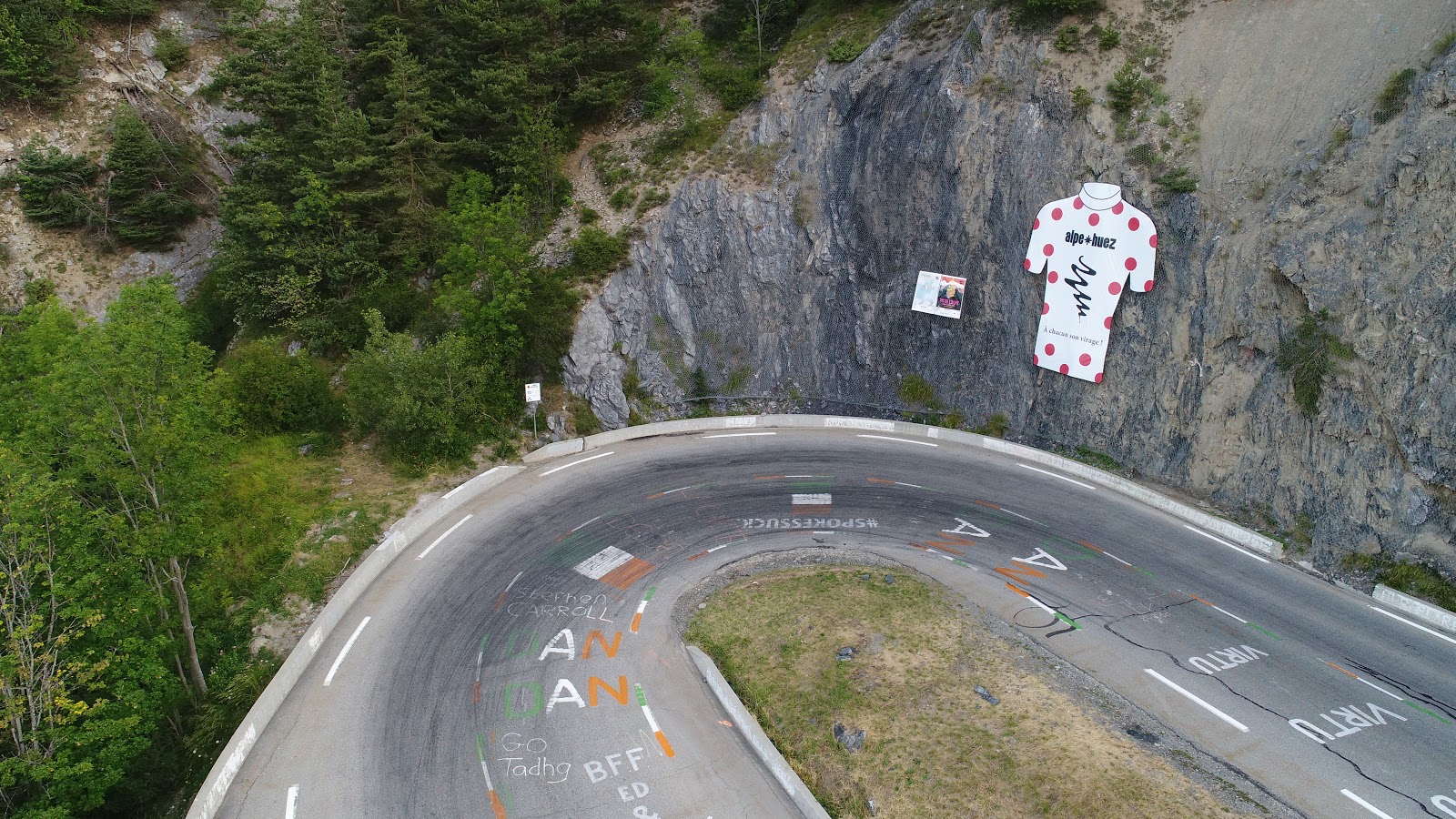 Bike climb Alpe d'Huez - turn (tornante) 10 aerial drone photo of mountain stage leader poster on wall and hairpin curve.