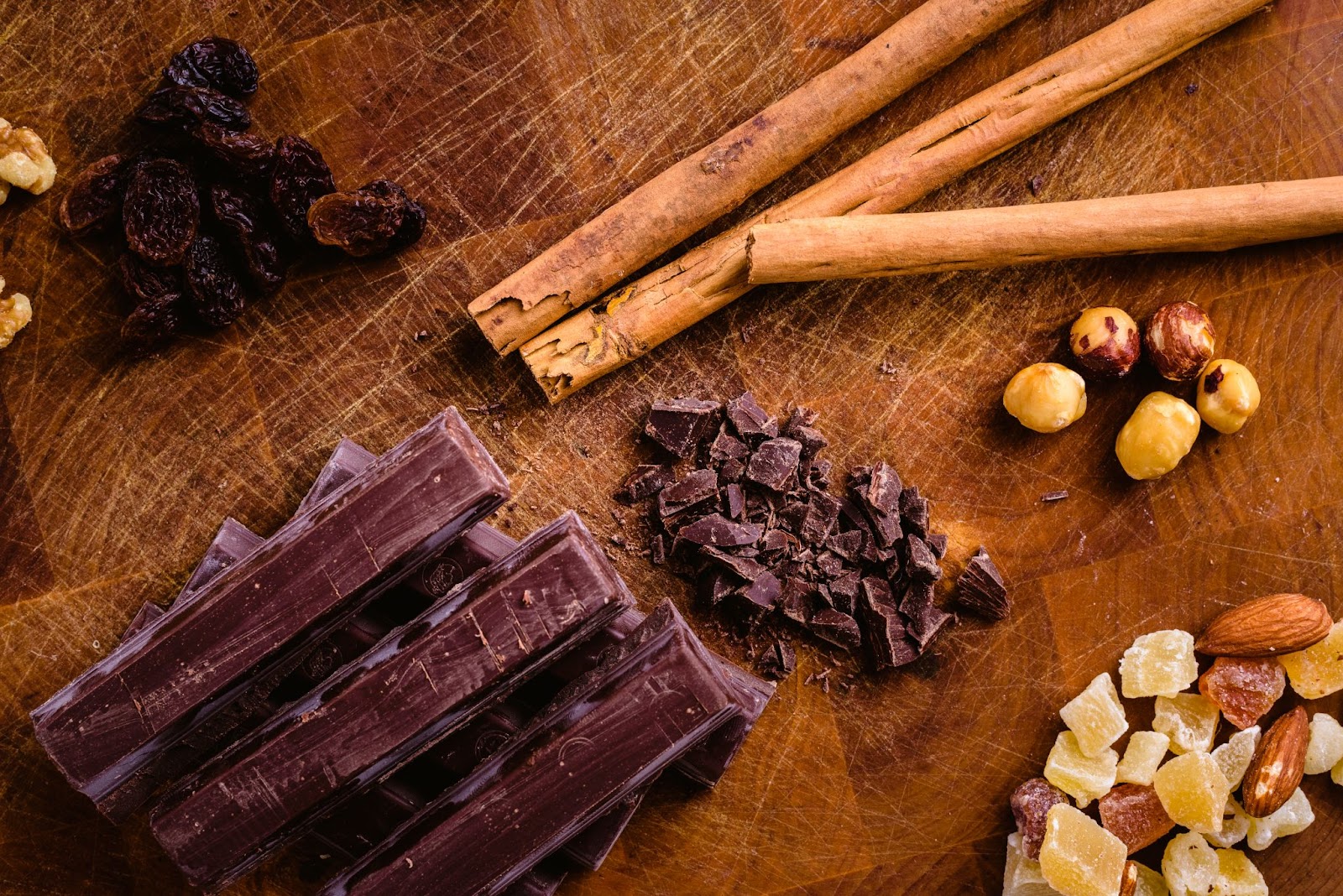 A plate adorned with dark chocolate chips and bars, complemented by cinnamon sticks, hazelnuts, and dried fruits.