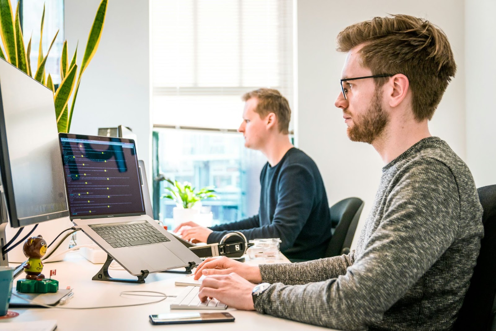 Two IT professionals working intently at their computers in a bright office.