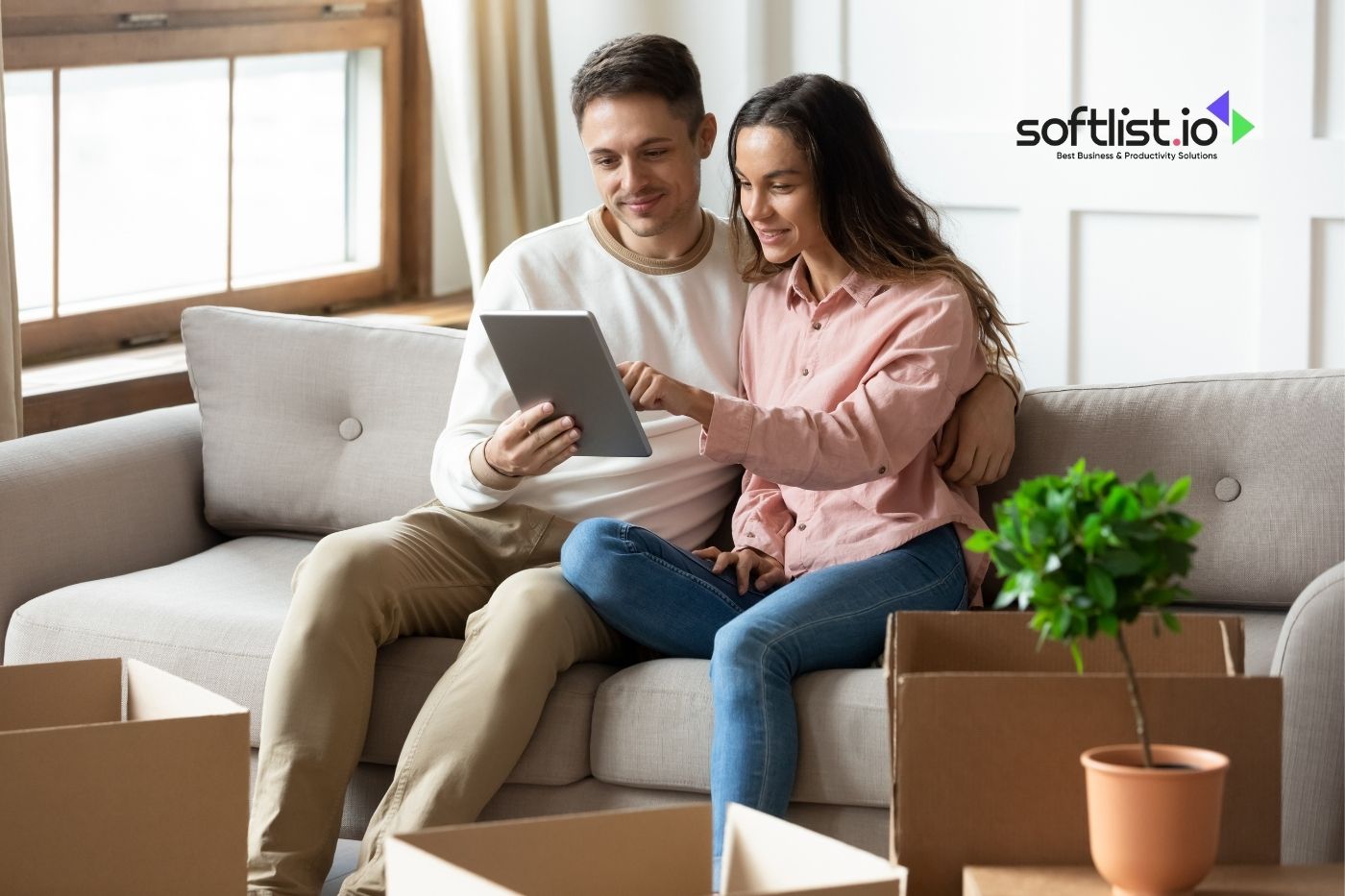 Couple looking at a tablet with softlist.io logo, moving boxes and plant in background.