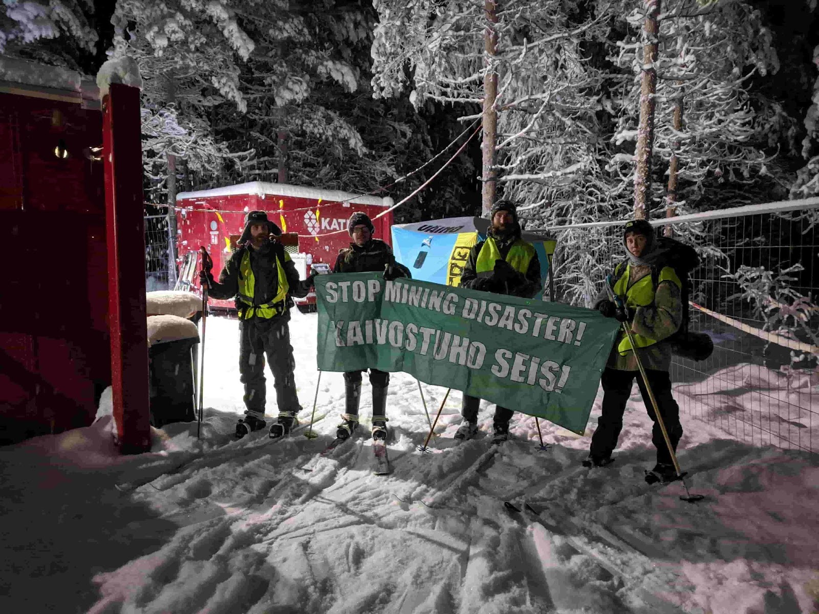 Rebels on skis stand outside a drill site holding a banner that says 'stop mining disaster!'