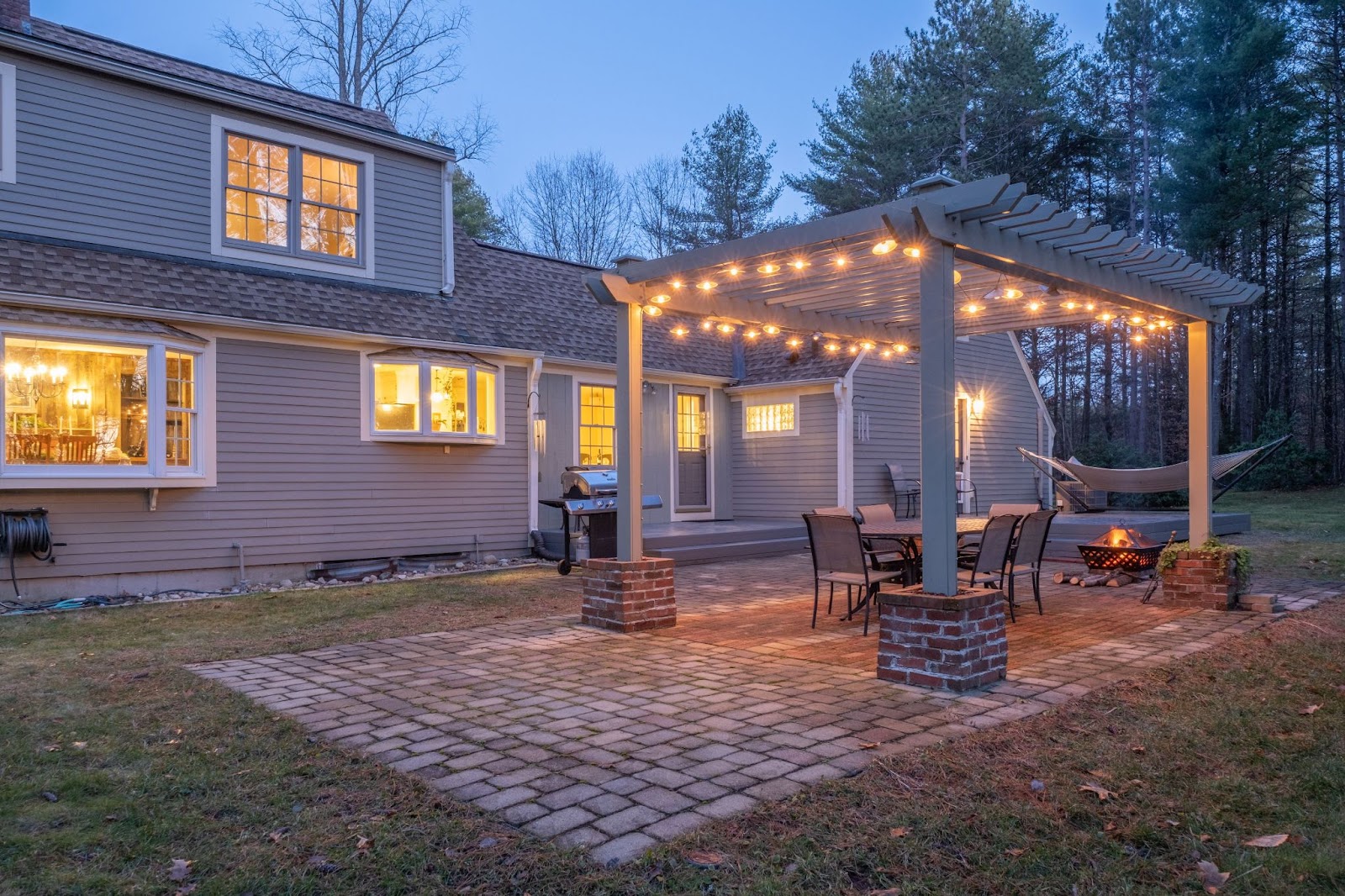 Outdoor view of a house and patio with string lights and a hammock at night. 