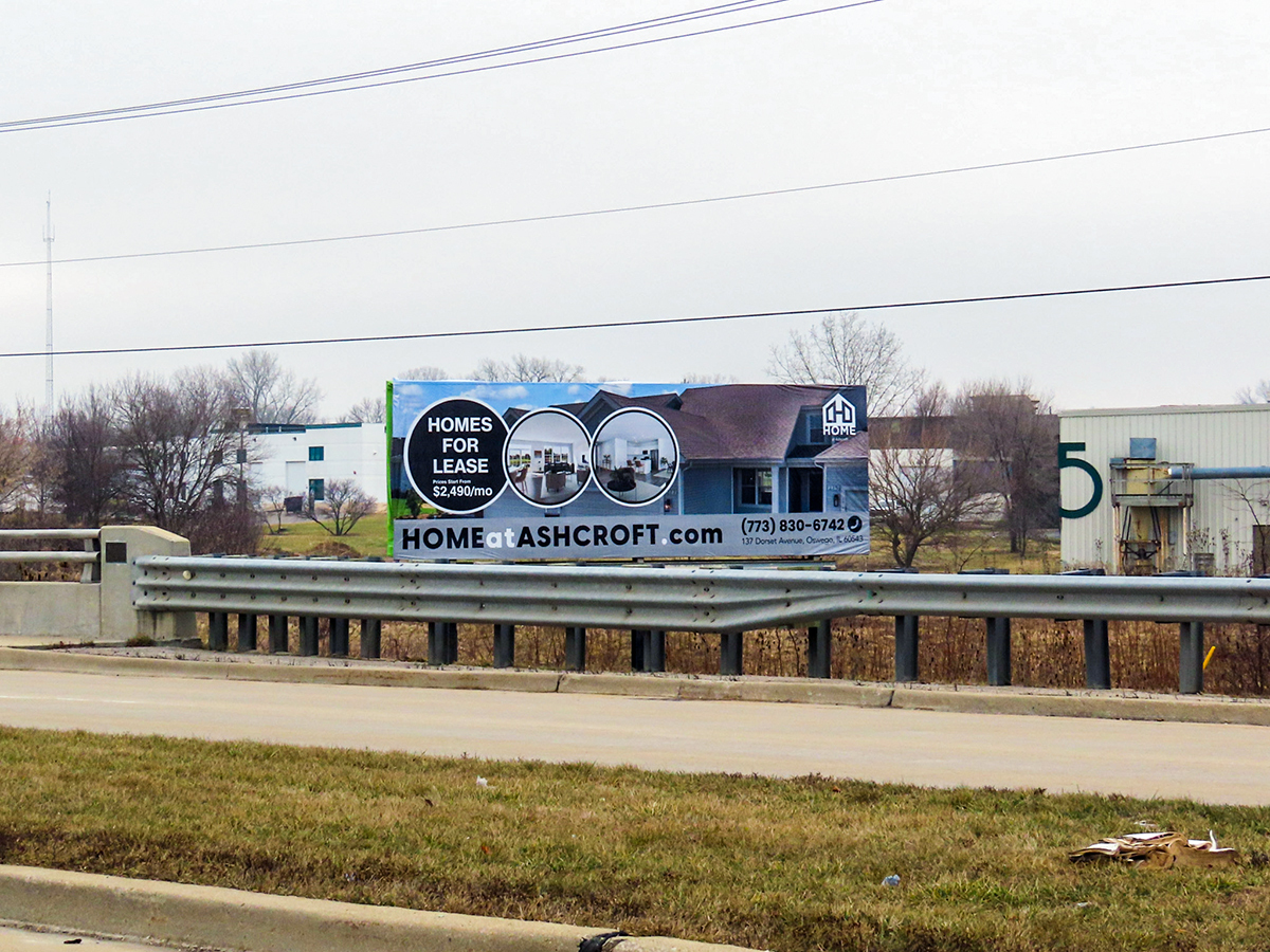 A real estate billboard along the highway depicting homes, a website, and a CTA.