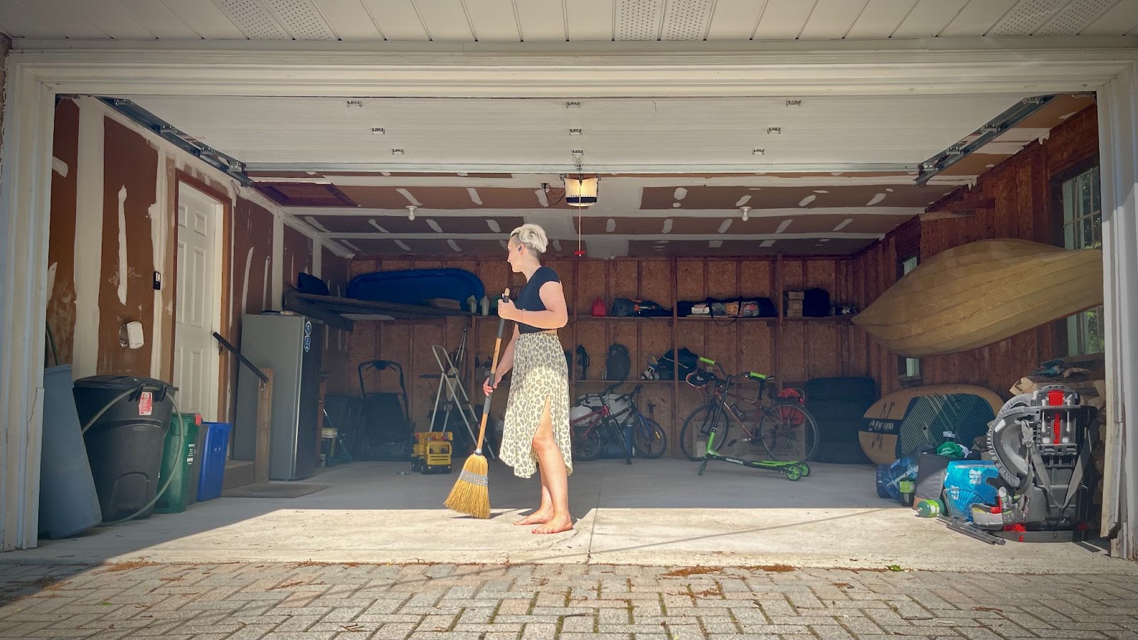 Tarzan takes a straw broom to the very clean floor of her tidy two-car garage. A canoe hangs on the side wall with a paddleboard below. There are several bikes and scooters all around her, a step ladder and a neat pile of items she has yet to bring to the dump and honestly probably won't for at least 3-6 months. She is wearing her signature summer outfit: a flowing zebra print skirt and simple black crop top.