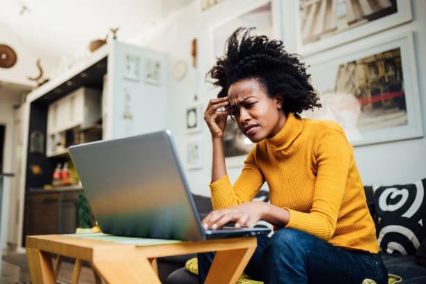 African American woman working from home Stressed out African American female freelancer working from home using her laptop and encountering some problems concerning her business IP Blocking stock pictures, royalty-free photos & images