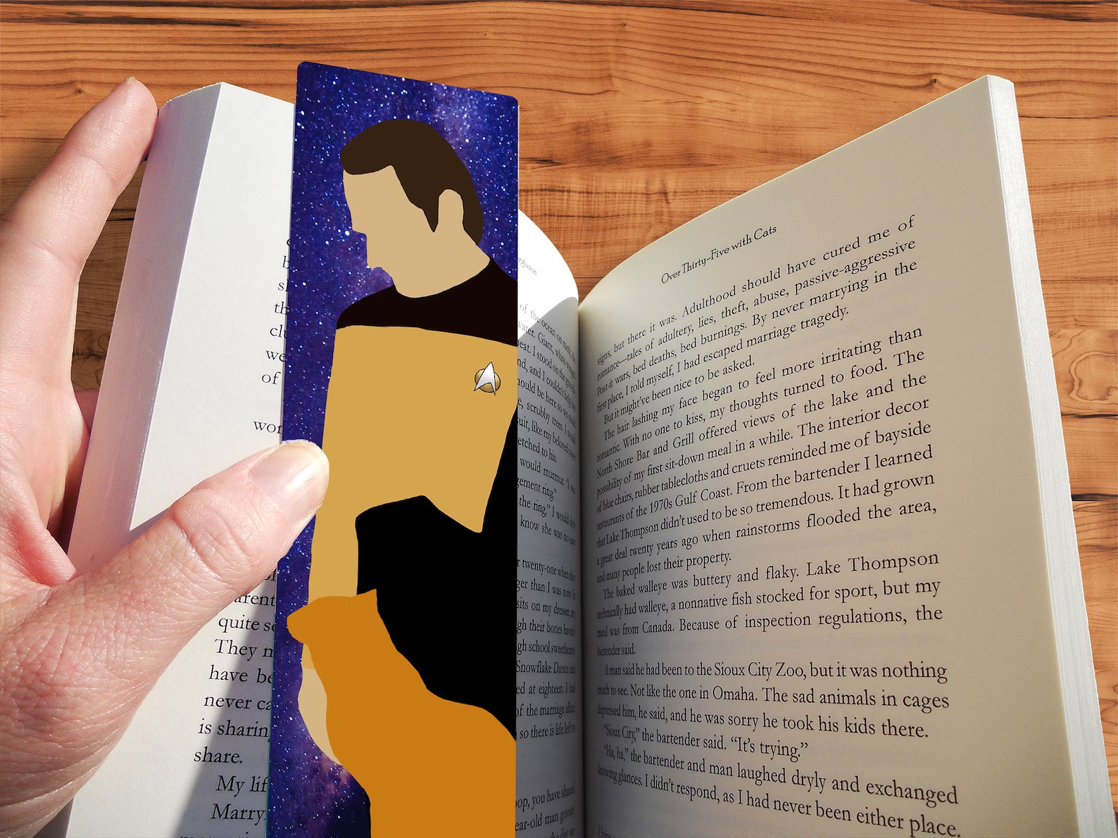 A minimalist bookmark inside a book showing silhouette art of Data from Star Trek, TNG series and an orange cat