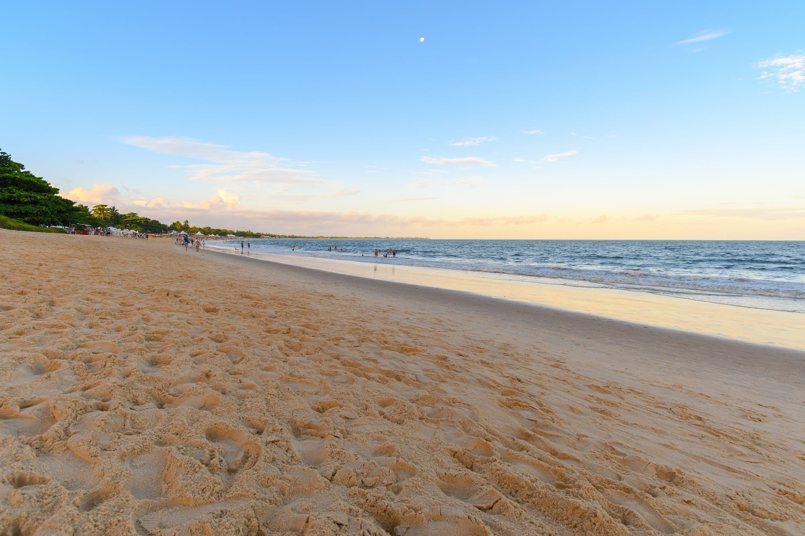 Areia da Praia de Taperapuã indo até o mar ao lado direito da imagem ao entardecer.