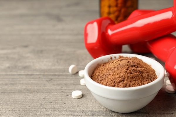 A small bowl of protein powder with tablet and dumbbells placed beside it