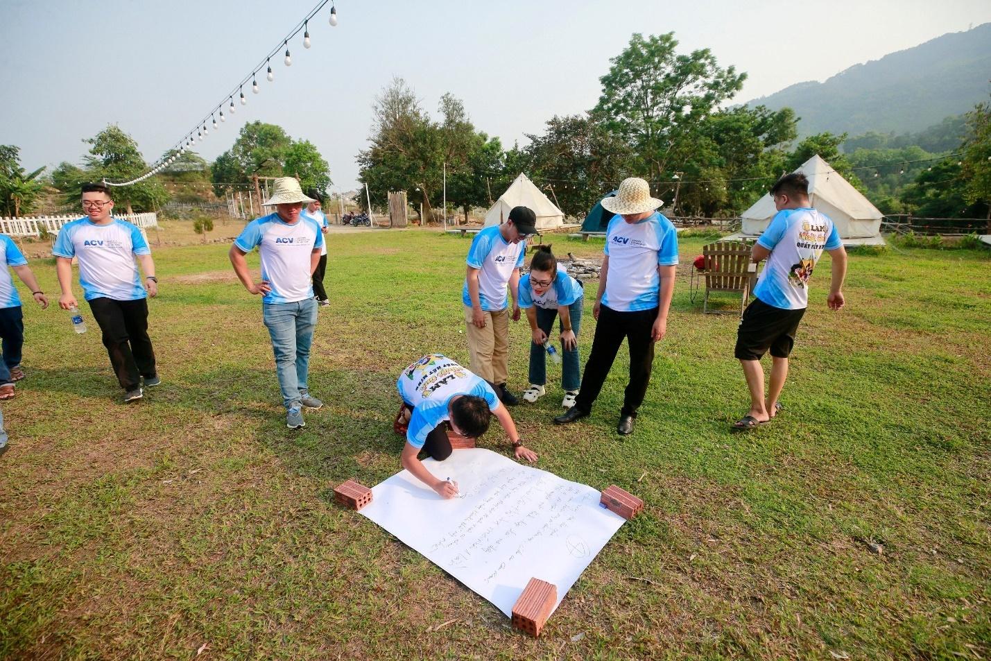 A group of people in a field writing on a large piece of paperDescription automatically generated