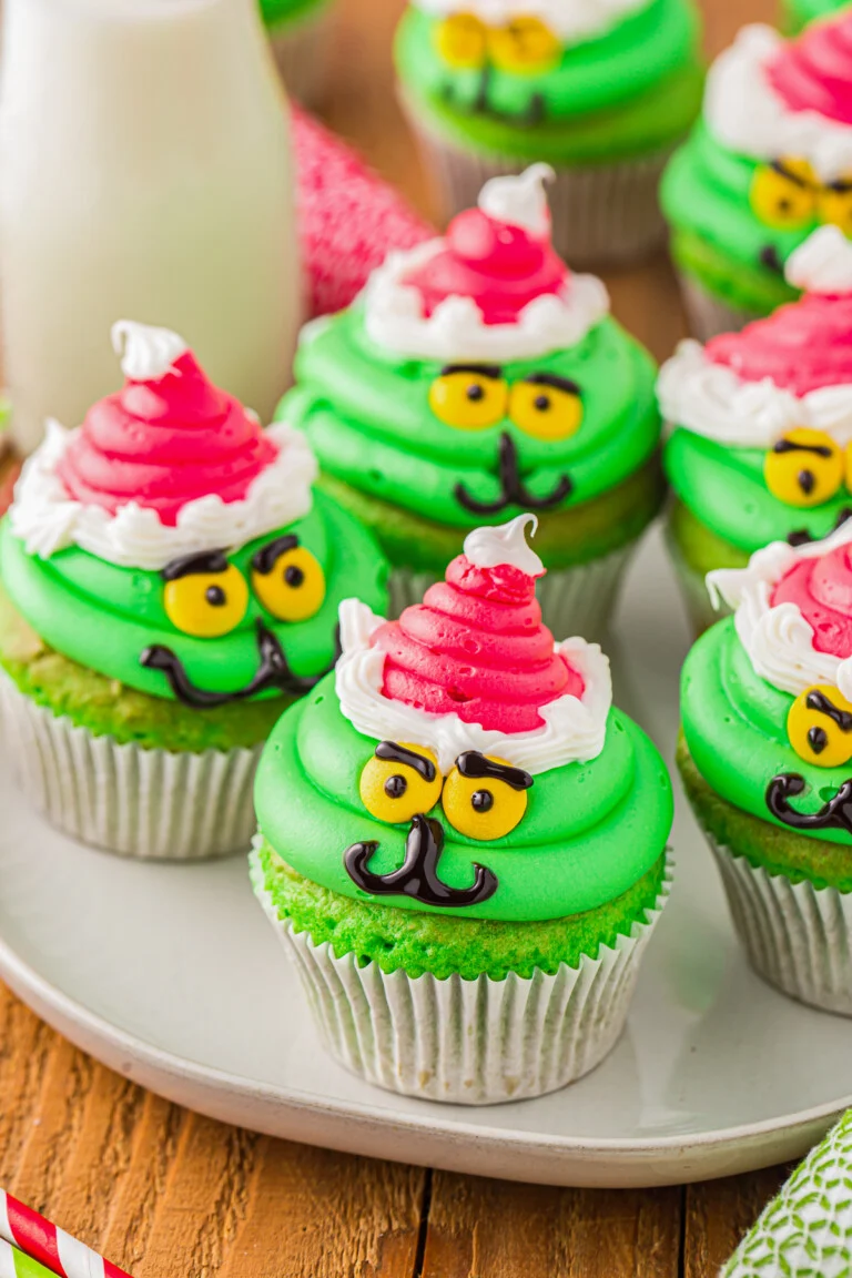 grinch cupcakes on white plate with santa hats and yellow eyes