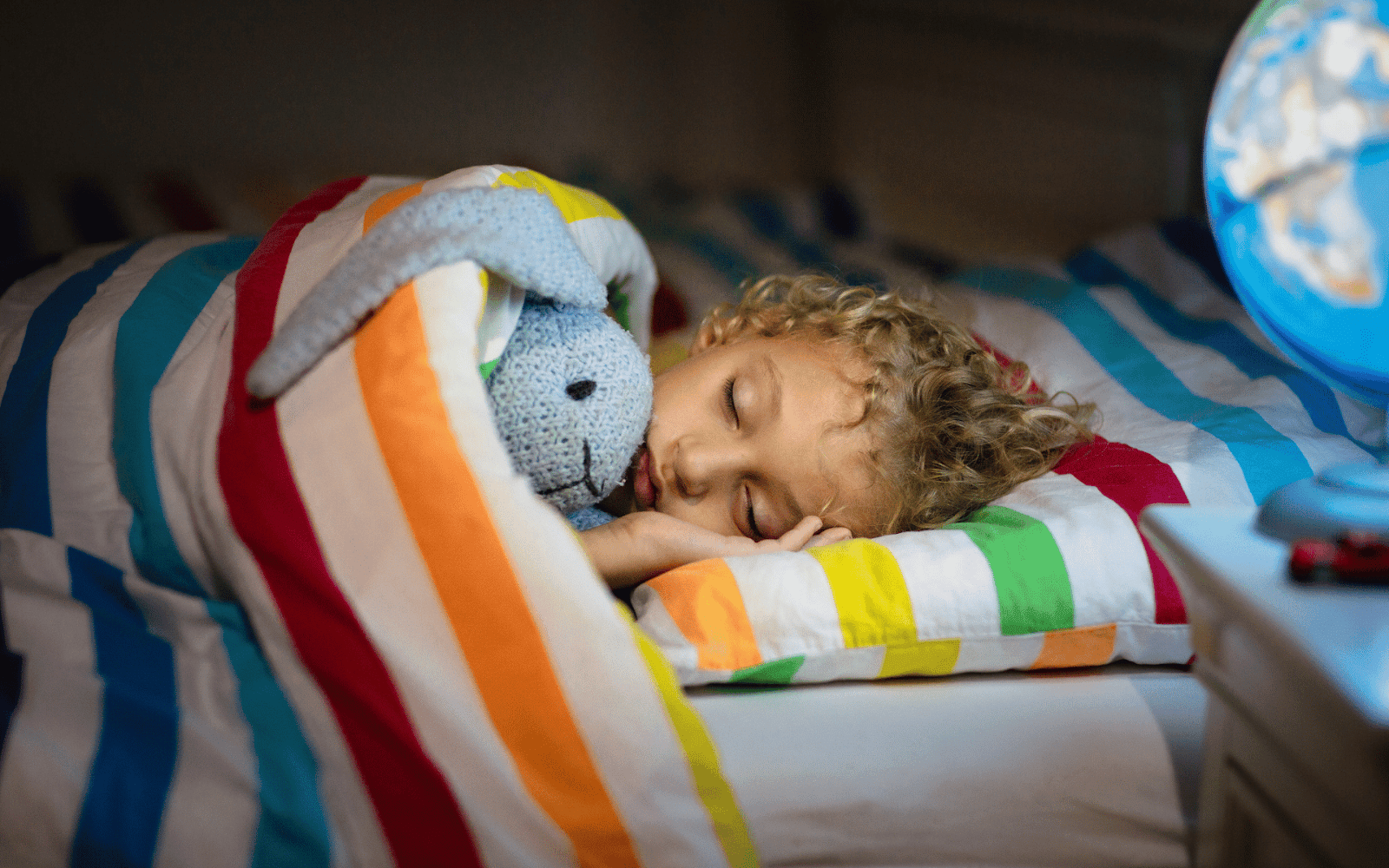 A child sleeping in a bed with a stuffed animalDescription automatically generated