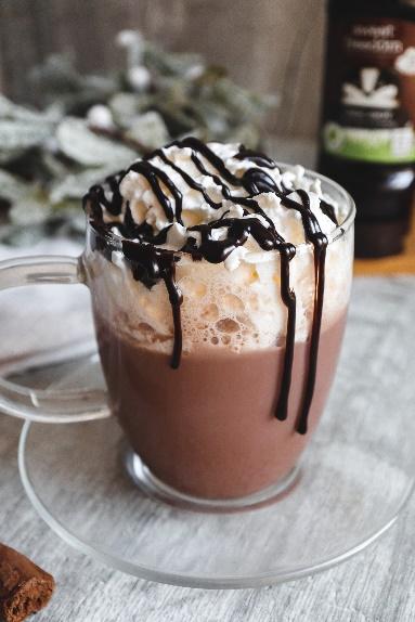 A glass cup of hot chocolate with whipped cream and chocolate syrup

Description automatically generated