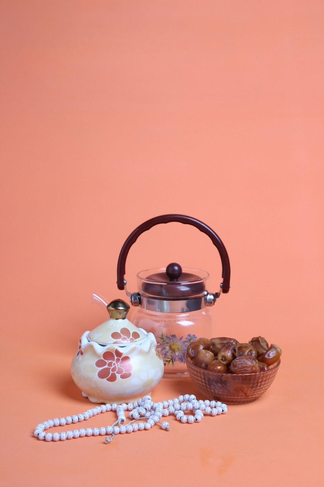 A tea kettle and a bowl of nuts on a pink background.

