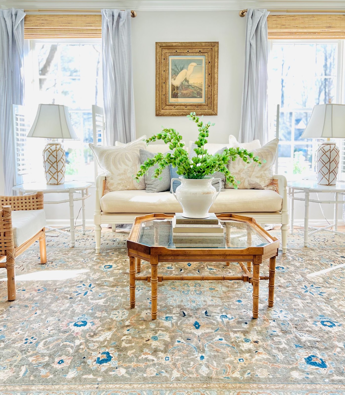 Sally's living room emanates a serene ambiance with its dominant white-beige color scheme, accented by touches of light brown on the coffee table, rattan armchairs, wall painting frame, area rug, and roller blinds.