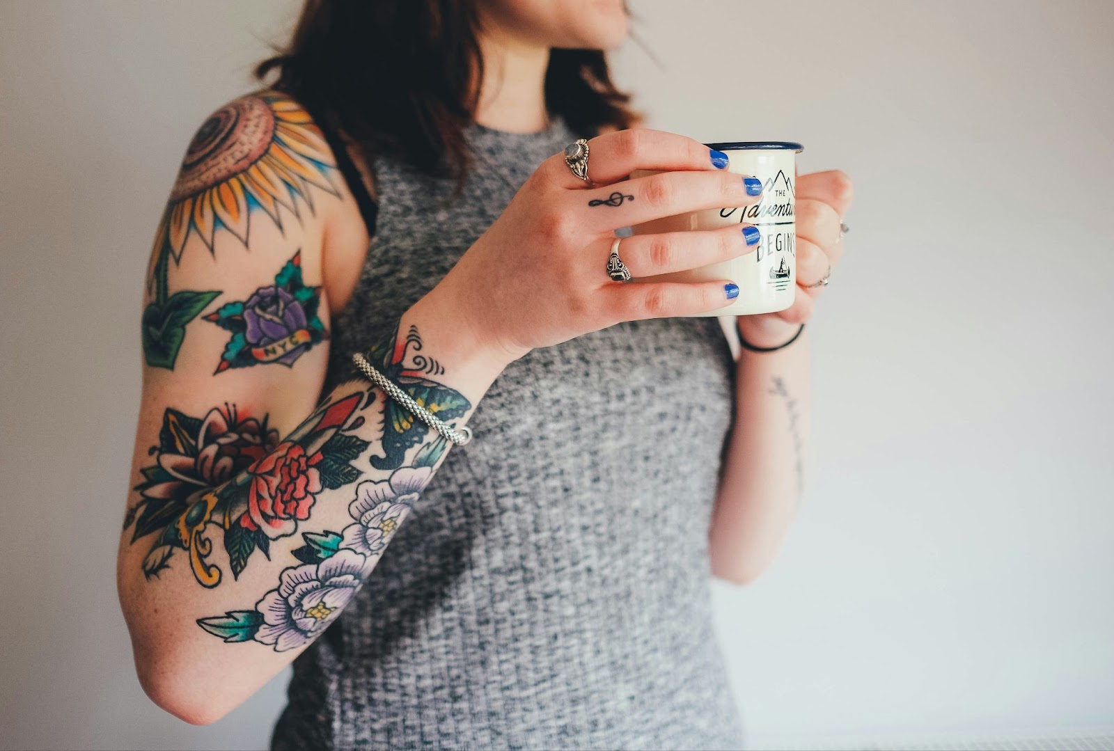 a closeup of a woman holding a coffee mug, with a tattoo sleeve done at a kelowna tattoo shop