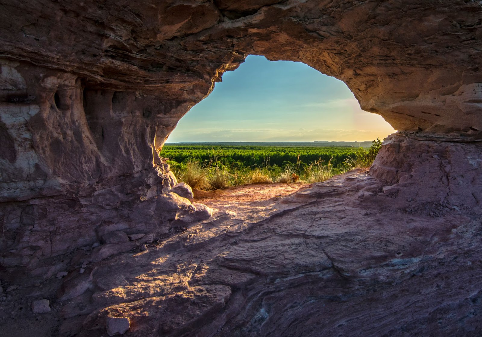 Foto da Pedra Furada no Jalapão. Formação rochosa com burado arredondado no meio. Através do buraco, paisagem do Parque Estadual do Jalapão ao entardecer.