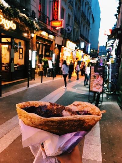 Someone holding a dessert crêpe on the street at night.